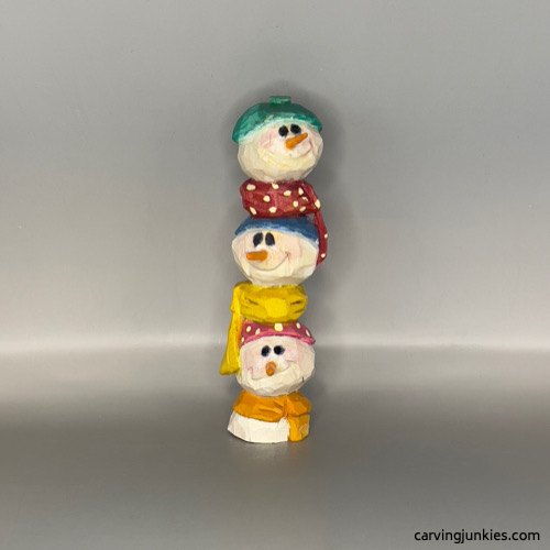 Three carved snowman faces stacked together with colorful hats and scarves
