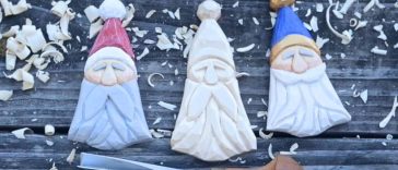 Three flat Scandinavian-style carved Santa ornaments on a dark wooden surface
