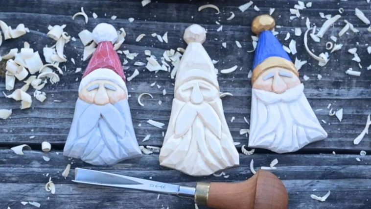 Three flat Scandinavian-style carved Santa ornaments on a dark wooden surface