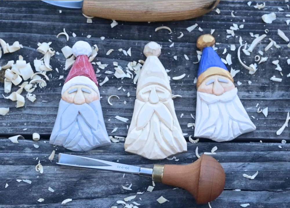 Three flat Scandinavian-style carved Santa ornaments on a dark wooden surface