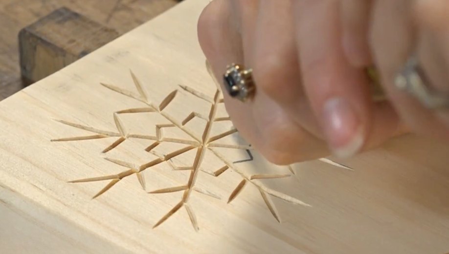 A V-tool carving a geometric snowflake into a flat wooden board