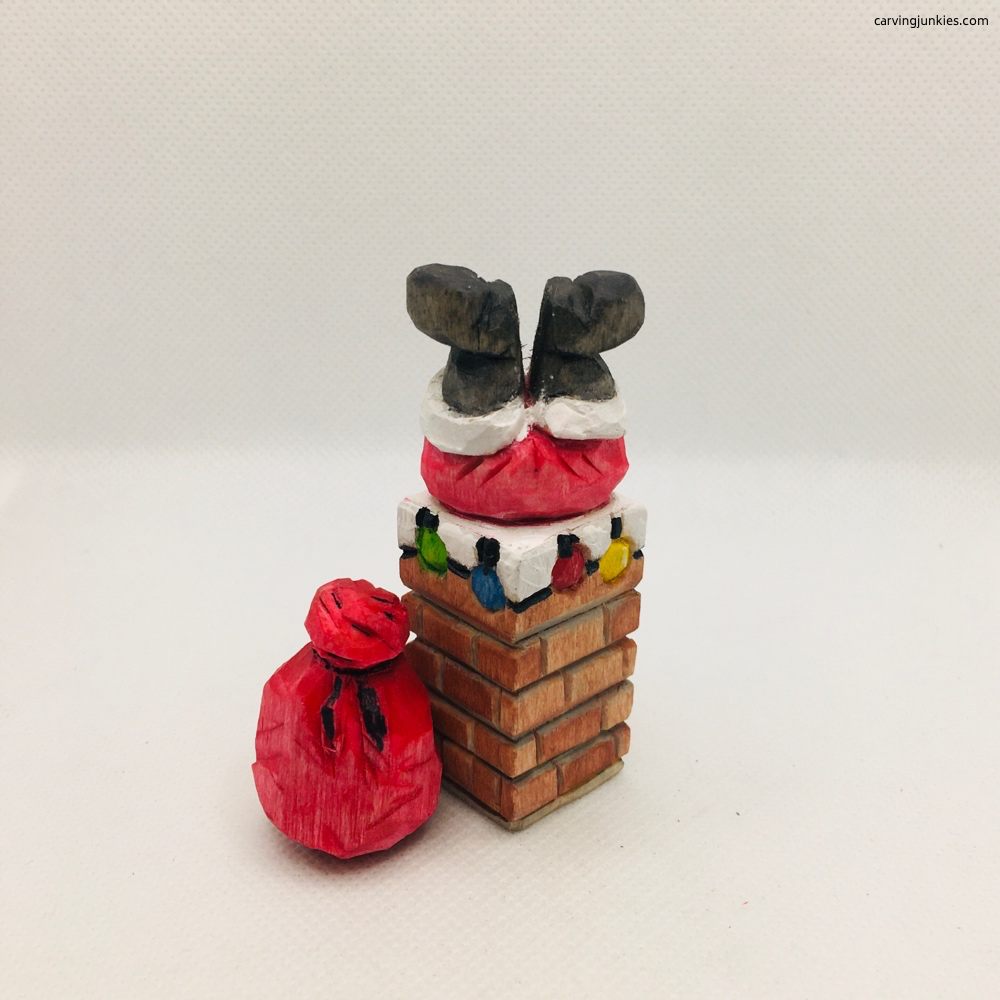 Santa boots sticking out of a carved brick chimney beside a red gift sack