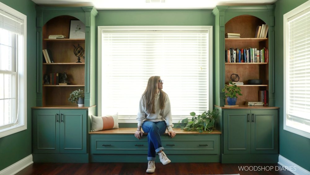 Green library cabinets and arched bookcases framing a window bench